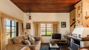 A cozy living room with a sofa, TV, fireplace, and windows with curtains. - Casa em Campos do Jordão com Lareira (Campos do Jordão)