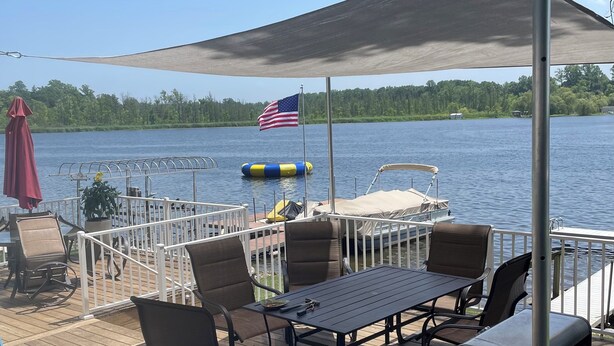 Una terraza con mobiliario exterior, una parrilla y vistas a un lago con un muelle y una bandera estadounidense.