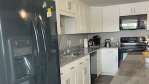 Una cocina moderna con gabinetes blancos, un refrigerador negro, un microondas y una estufa.