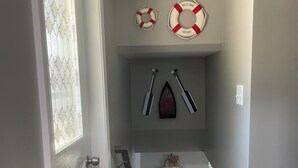 Un pasillo con una puerta, un salvavidas colgado en la pared, una pala y un cartel de bienvenida.