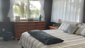 Un dormitorio con cama, cómoda, mesita de noche, lámpara y ventana con cortinas.