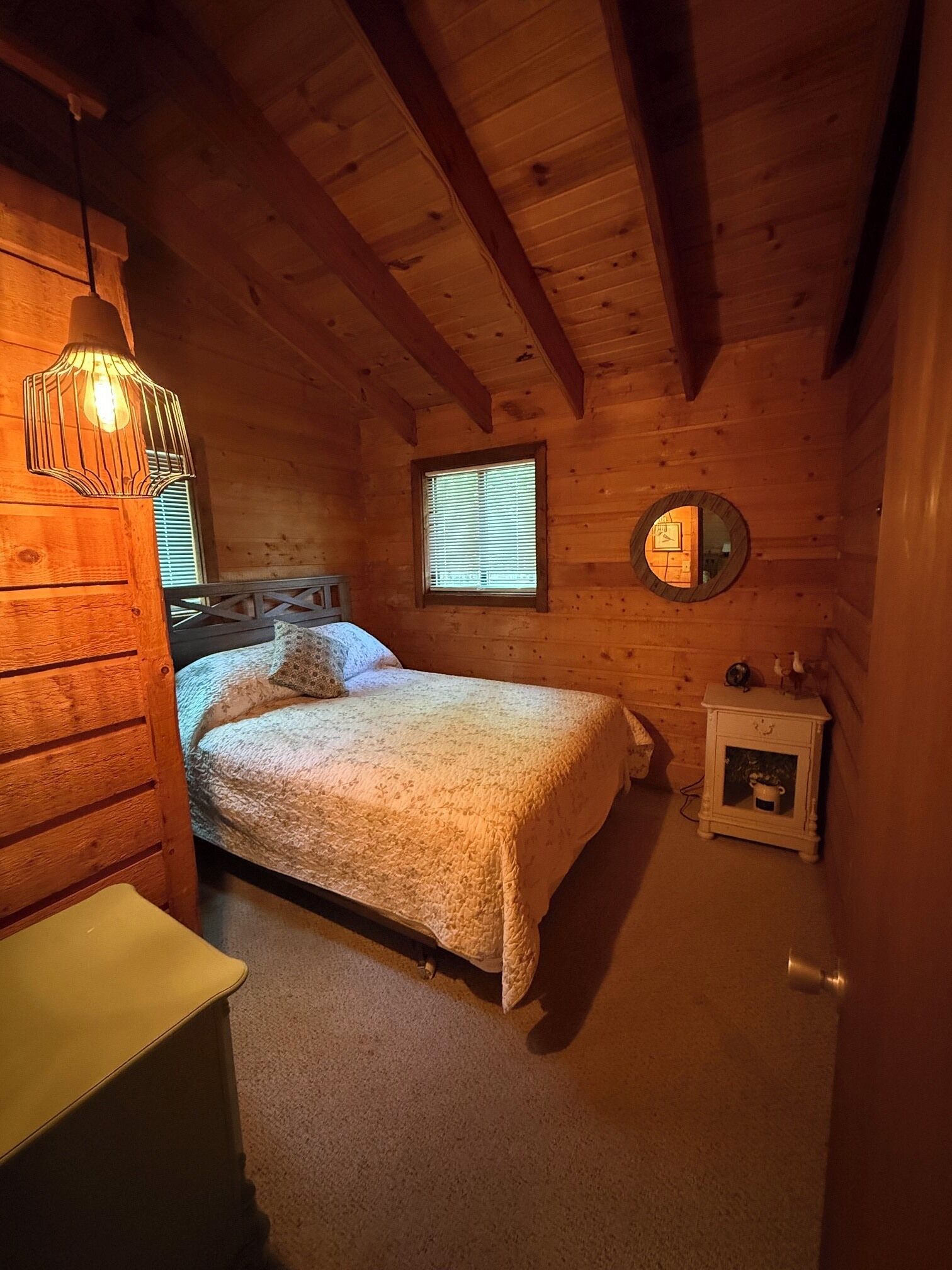 Een knus slaapkamer met een bed, een nachtkastje, een lamp en een kleine klok aan de muur.