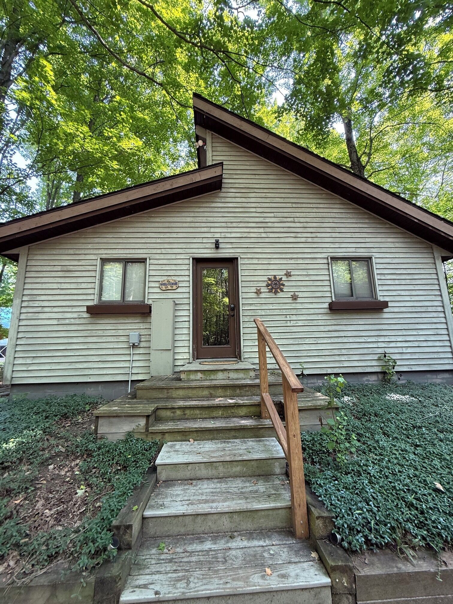 A two-story house with a front porch, wooden steps, and a small garden area.
