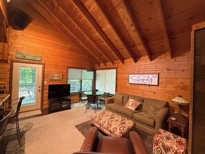 Interior acogedor de una cabaña de madera con televisor, sofá y zona de comedor.