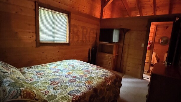 A bedroom with a bed, a window, and a wooden ceiling.