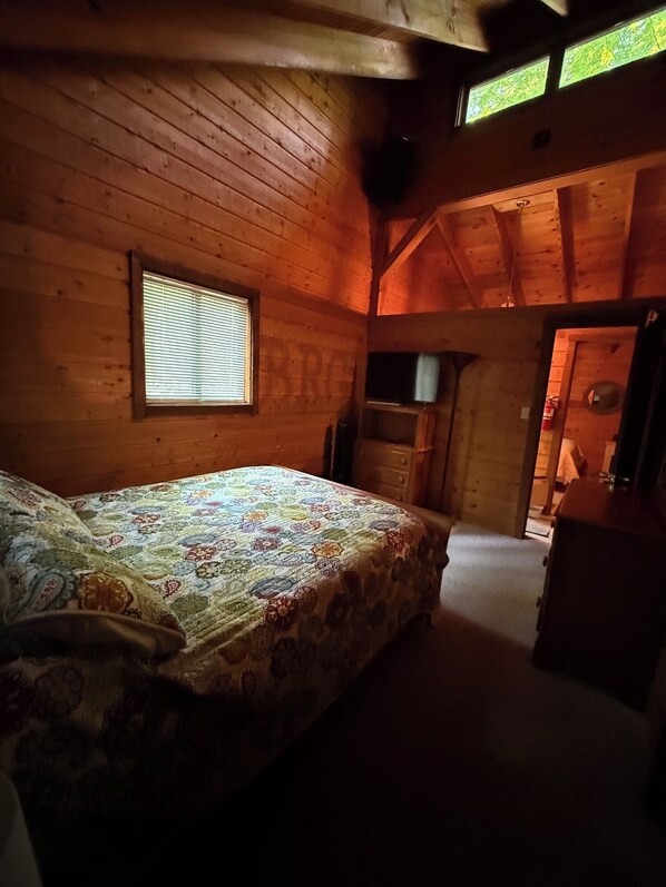 A bedroom with a bed, a window, and a wooden ceiling.