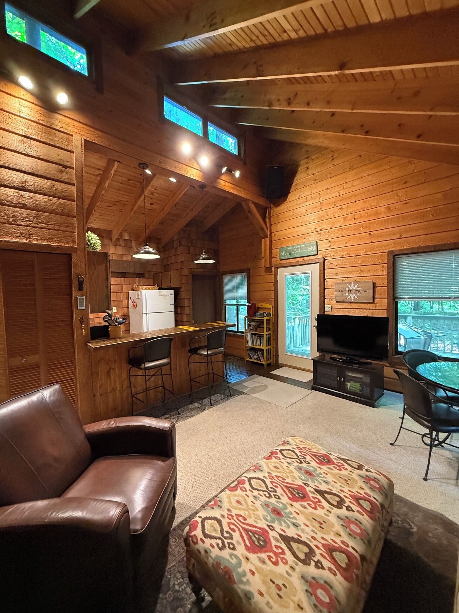 Interior acogedor de una cabaña de madera con barra, asientos y televisor.