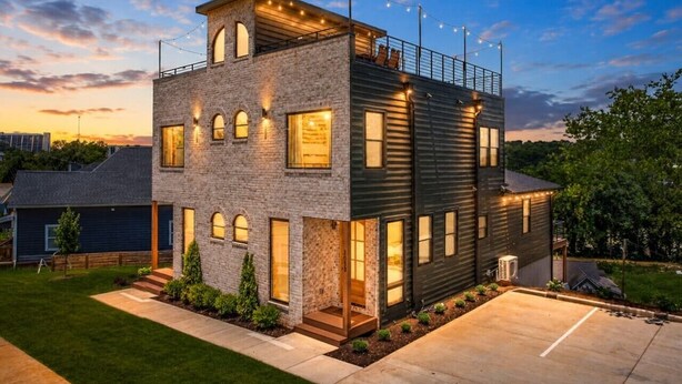 Una casa moderna de dos pisos con fachada de piedra, ventanas amplias y un garaje visible.