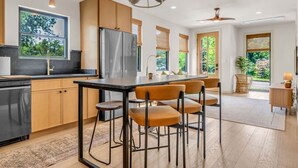 Una cocina moderna con una isla central, taburetes de bar y un comedor con vistas a zonas verdes.