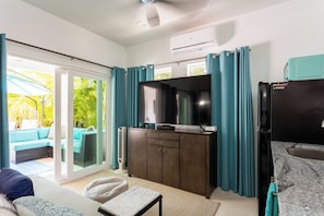 Uma sala de estar moderna com um sofá, uma TV, um armário e uma porta de vidro deslizante que dá para uma varanda.