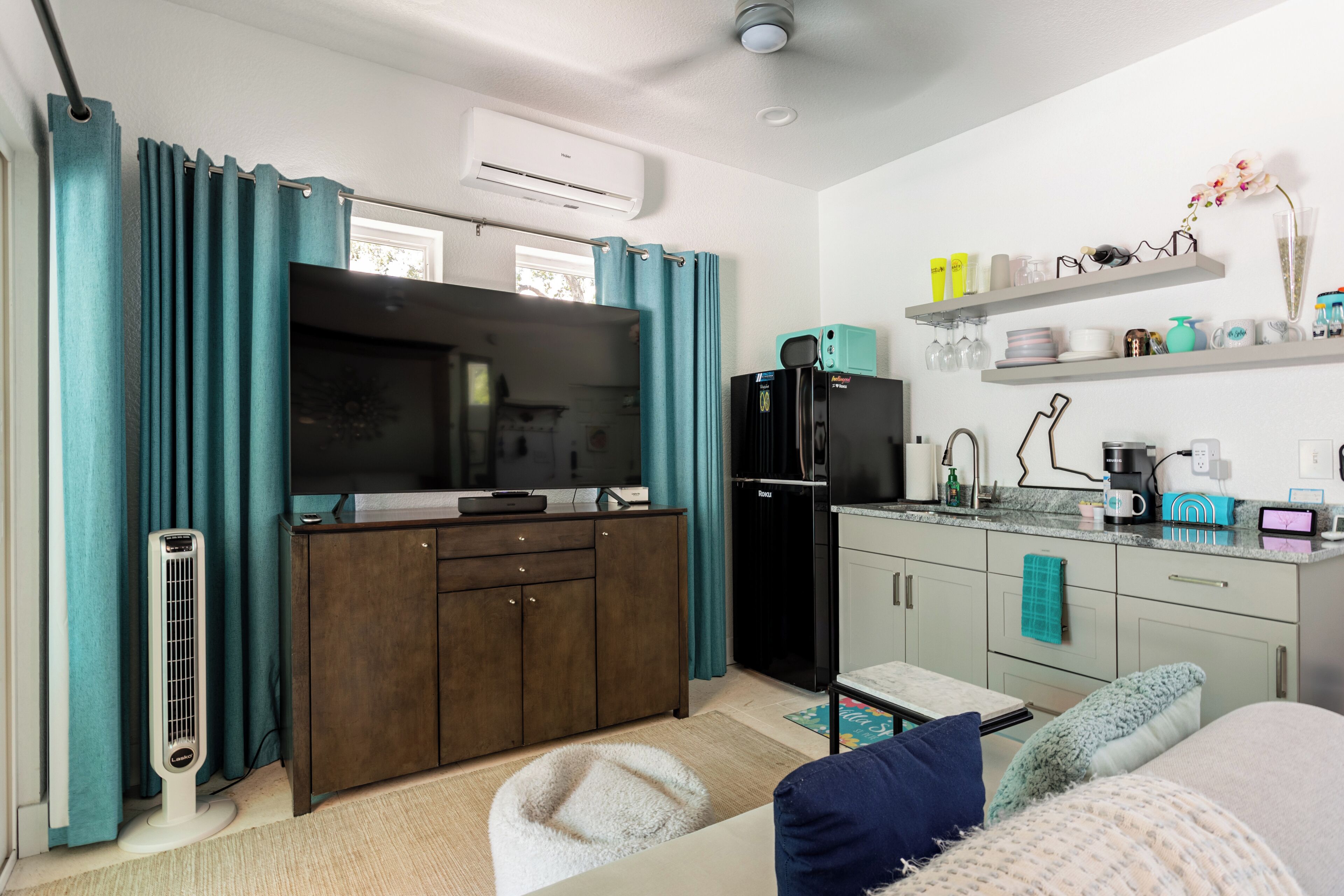 A compact kitchen with a built-in oven, a refrigerator, and a microwave. There is a dining table with chairs, a sofa, and a small rug.