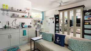Een moderne keuken met een ingebouwde oven, een koffieapparaat en een spoelbak. Er is een eethoek met een tafel en stoelen, en een bank met kussens.
