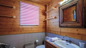 Puisesta mökistä löytyvä kylpyhuone, jossa on wc, pesuallas ja ikkuna, jossa on raidalliset sälekaihtimet.