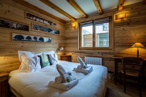 A wooden cabin room with a bed, towels, a chair, and framed pictures on the walls. - Chalet Paradis Blanc - 3 bedroom chalet near the golf course (Chamonix-Mont-Blanc)