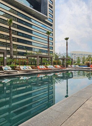 Ein modernes Hotel mit Poolbereich, Liegestühlen und Palmen.