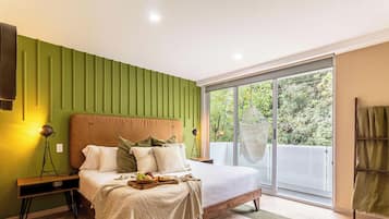 A bedroom with a bed, bedside table, lamp, and a view of greenery through a sliding glass door.