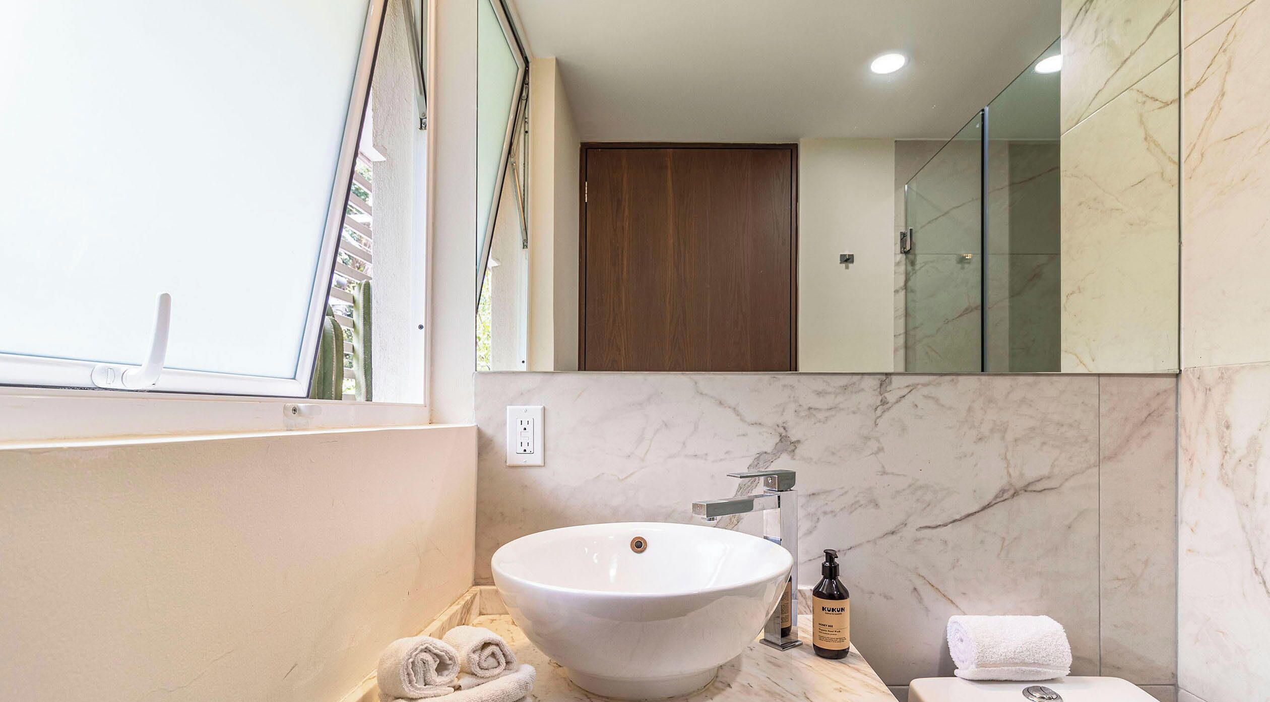 A bathroom with a white vessel sink, a wooden door, and a glass shower enclosure.