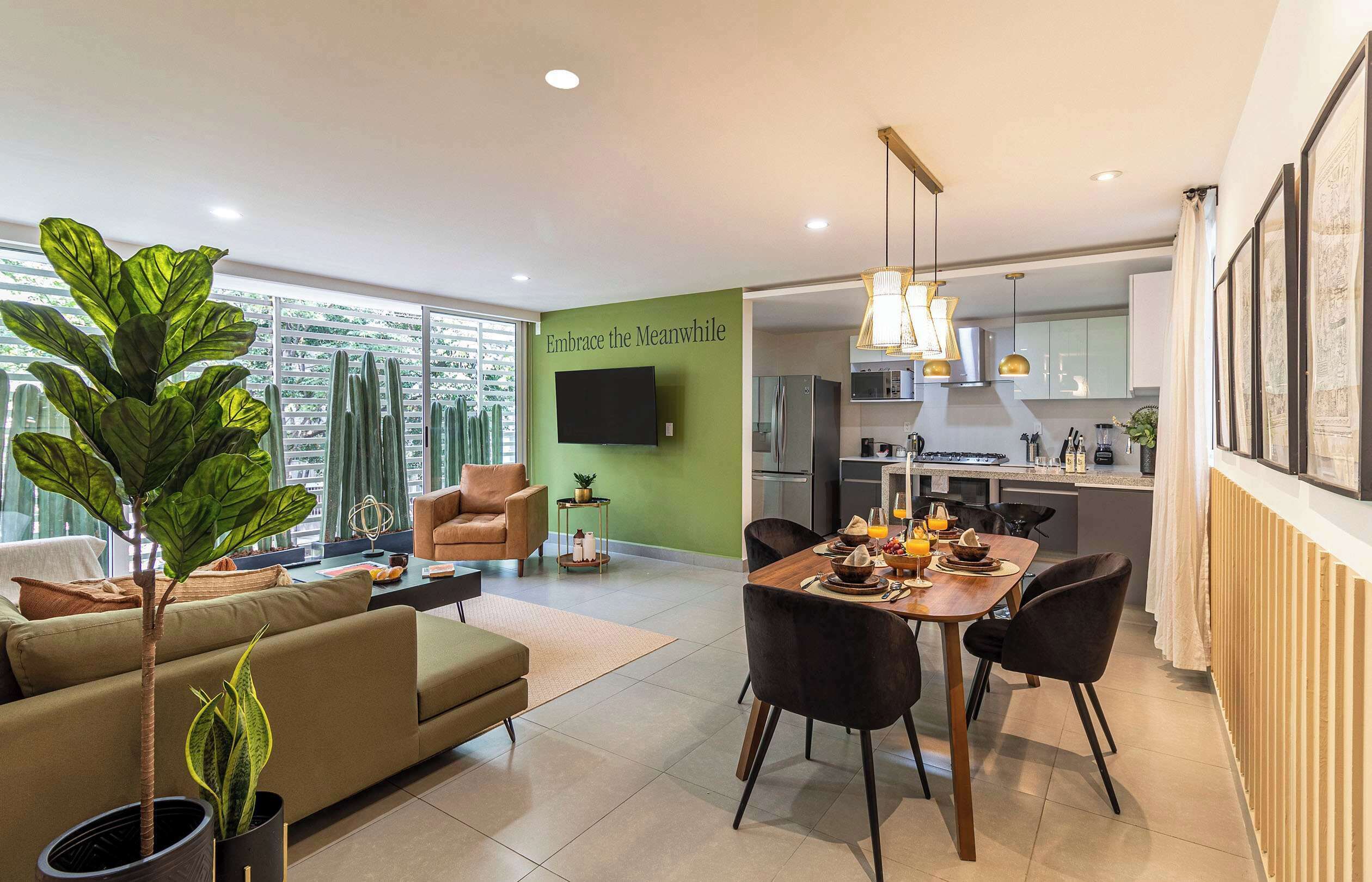 A modern living room with a sofa, a dining table set for two, and a kitchen in the background.