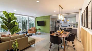 A modern living room with a sofa, a dining table set for two, and a kitchen in the background.