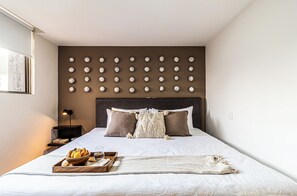 Ein ordentlich bezogenes Bett mit einem Frühstücksbrett, einer Nachttischlampe und einer an der Wand befestigten Uhr.