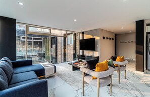A modern living room with a sofa, coffee table, and armchairs, a flat-screen TV, and a large window offering a city view. - Casa Horacio by Kukun (Ciudad de México)