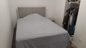 A small, single-bed room with a plain headboard, a bedside table with a lamp, and a clothing rack against the wall. - Apartment in the village of Tomino, 10 minutes from the sea and Macingaggio. (Tomino)