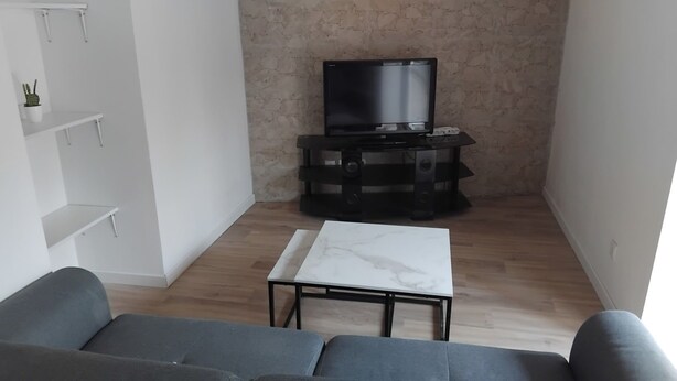 A living room with a sofa, a small table, a TV on a stand, and a brick wall. - Apartment in the village of Tomino, 10 minutes from the sea and Macingaggio. (Tomino)