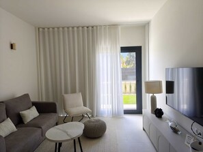 Ein modernes Wohnzimmer mit einem grauen Sofa, einem runden Couchtisch, einem weißen Sessel, einem Fernseher und einer Lampe.