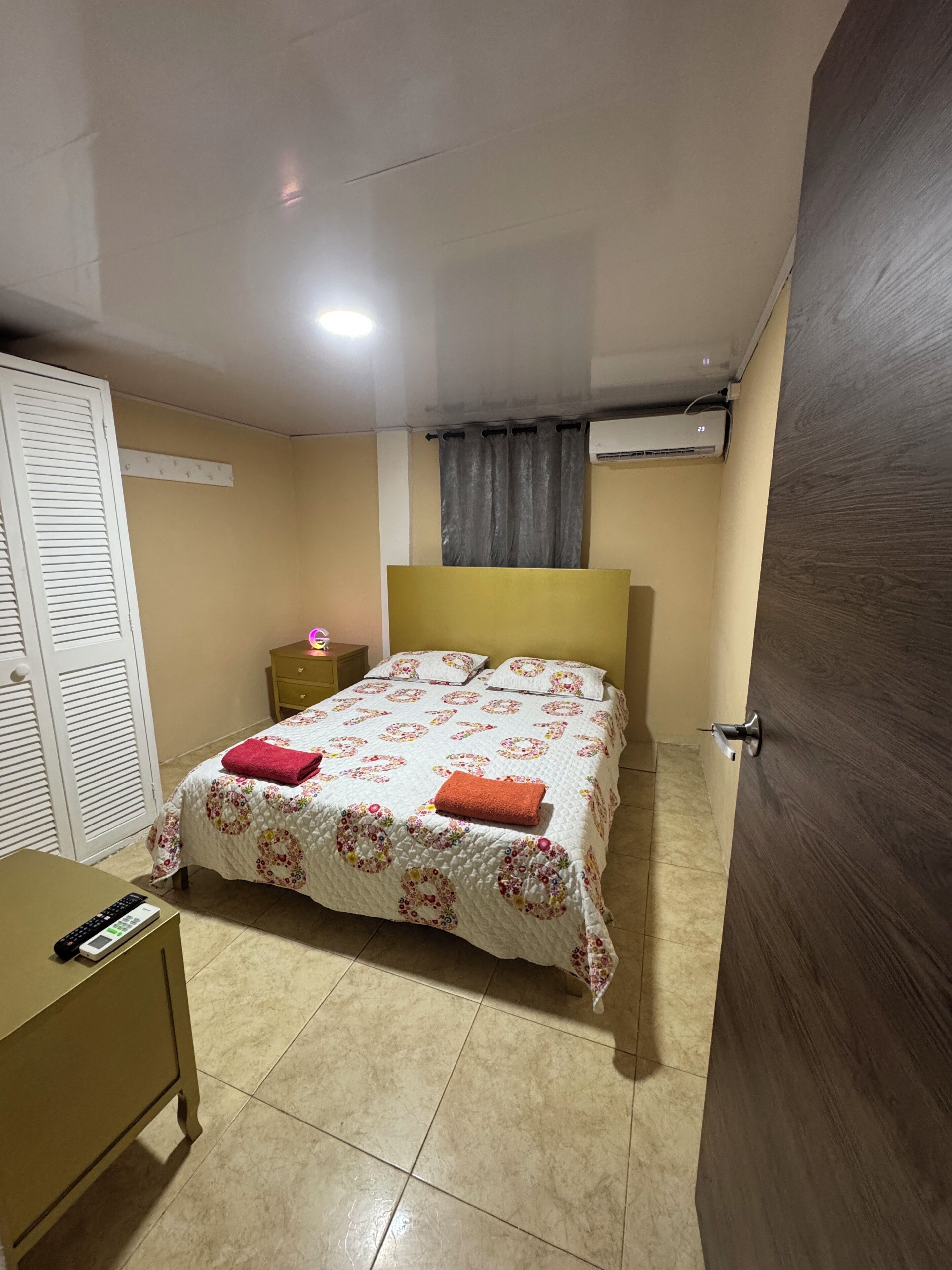Un dormitorio con cama, mesita de noche, armario y aire acondicionado.