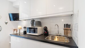 Et moderne køkken med hvide skabe, en sort bordplade, en mikrobølgeovn, kaffemaskine og en rustfri stålvask.