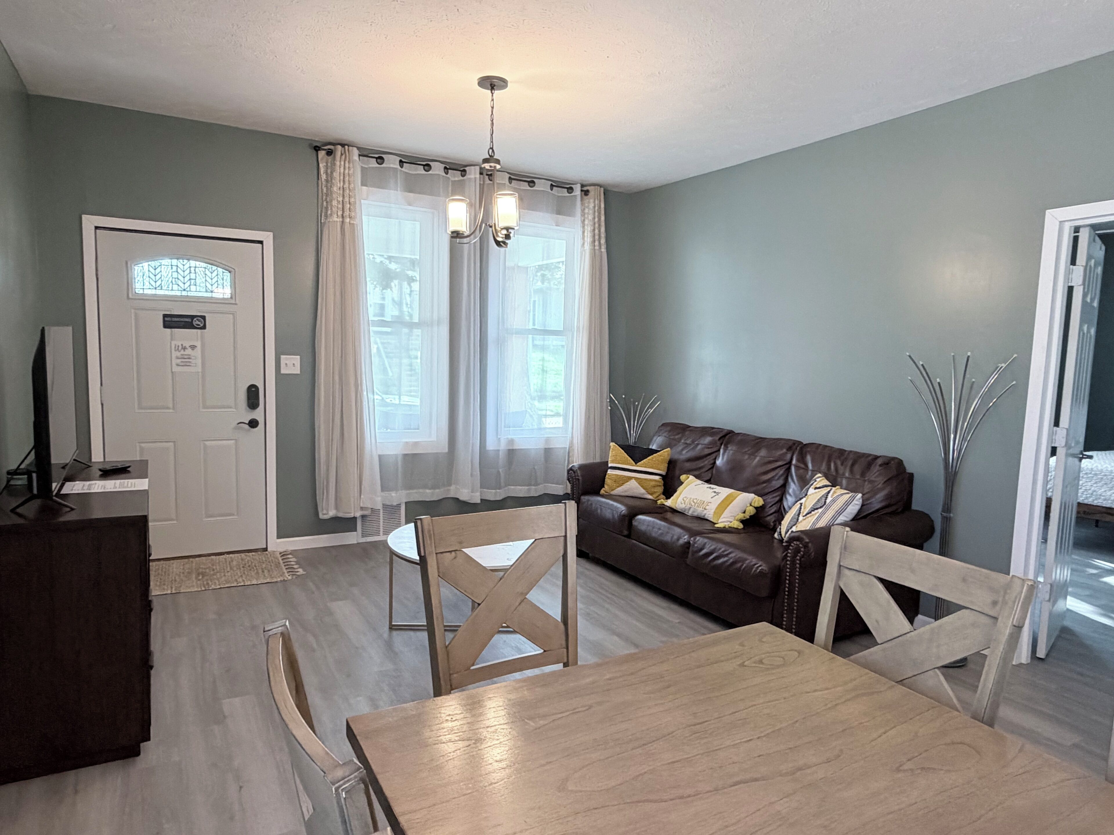 A living room with a brown leather sofa, a wooden dining table, and a white door with a window.
