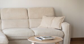 A beige upholstered sofa with a cushion, a small round table with books, and a plain wall in the background. - Loft atelier 120m2 - duplex - Bois de Vincennes (Fontenay-sous-Bois)