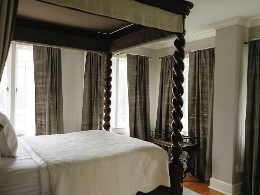 A four-poster bed in a room with large windows and curtains.