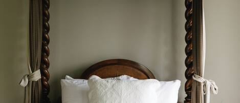 Un lit avec une tête de lit en bois, une literie blanche et des rideaux attachés.