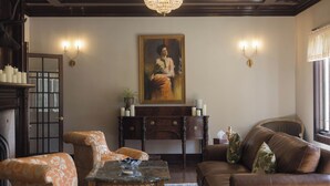 Ein Zimmer mit einer Couch, einem Sessel, einem Tisch, einem Gemälde und einer Chandelier.