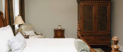 Quarto com cama, guarda-roupa de madeira, mesa de cabeceira e uma cadeira.