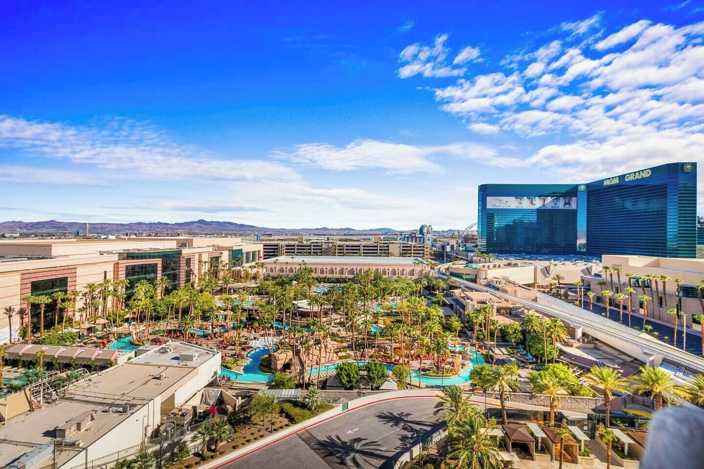 A resort with multiple swimming pools, palm trees, and a view of the Grand Casino.