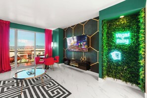 Una sala moderna con un televisor grande, sillas rojas, una mesa de centro de vidrio y un letrero de neón que dice 'Vegas Baby'.