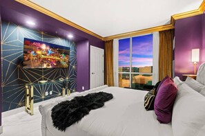 A hotel room with a large bed, a TV mounted on the wall, and a view of the cityscape through the window.