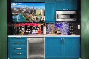 Cocina con gabinetes color turquesa, refrigerador de acero inoxidable, microondas y televisor que muestra un paisaje urbano.