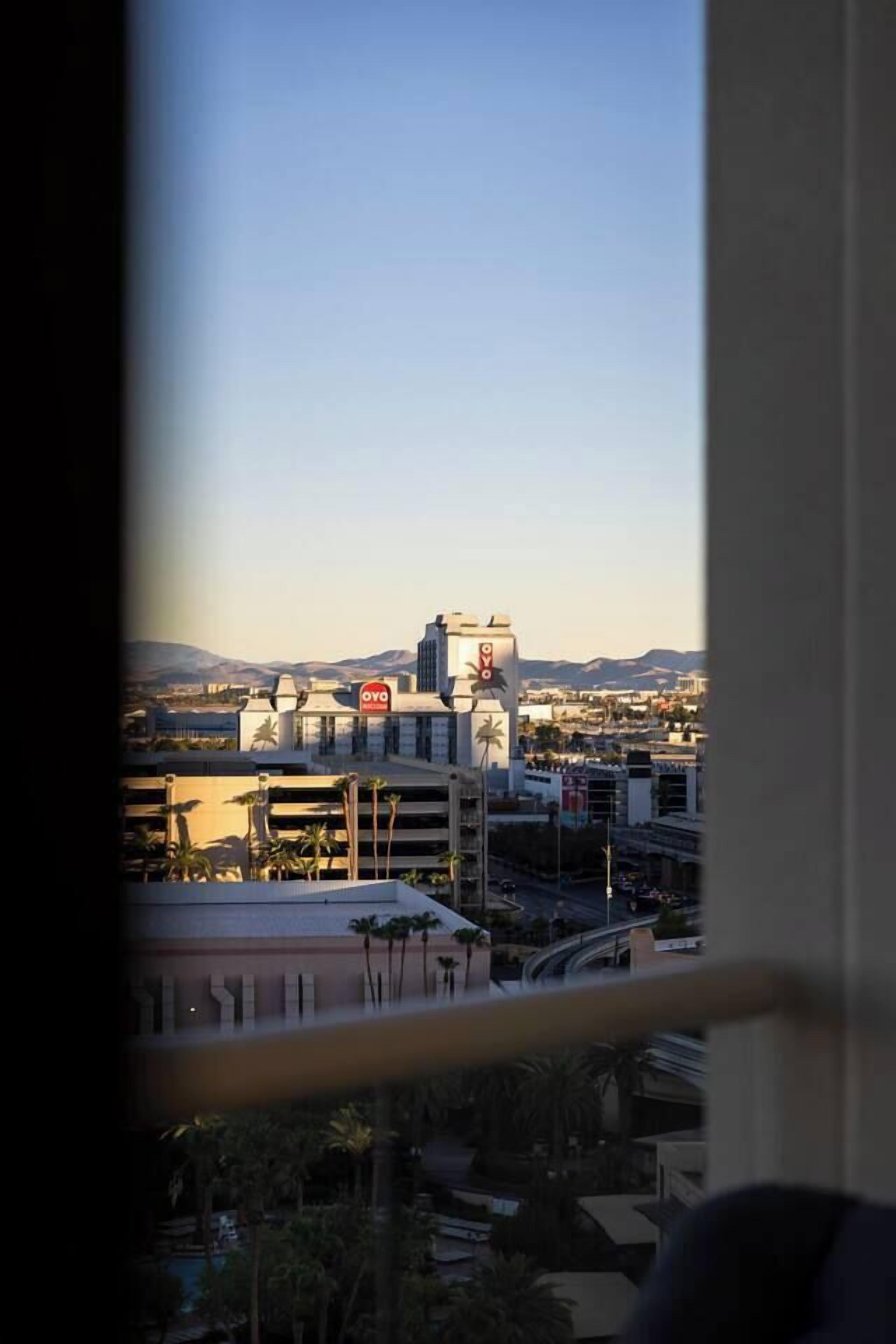 Vista de un paisaje urbano a través de una ventana, con un edificio destacado que muestra un letrero con la palabra 'OVO'.