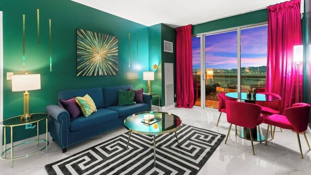 Een moderne woonkamer met een blauwe bank, een glazen salontafel en uitzicht op het landschap door grote ramen.