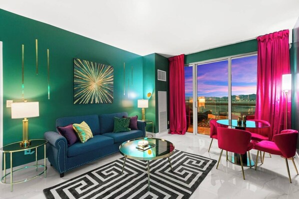 A modern living room with a blue sofa, a glass coffee table, and a view of the outdoors through large windows.