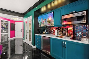 A modern kitchen with teal cabinetry, a stainless steel oven, and a cityscape painting above the counter.