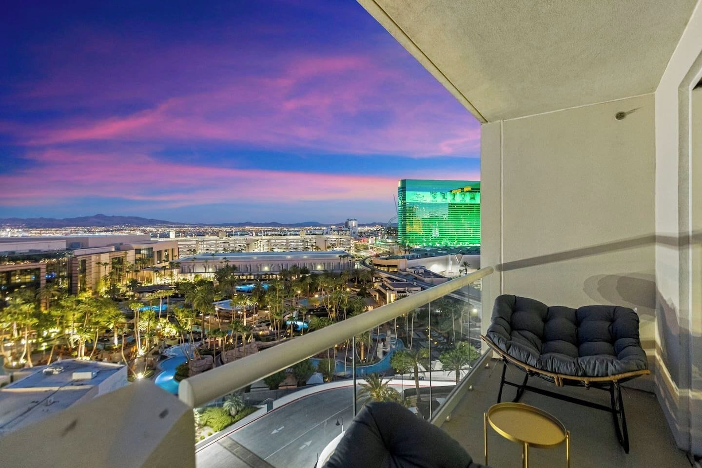 A balcony with a view of a cityscape, including a hotel and a green-lit building.