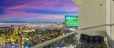 A balcony with a view of a cityscape, including a hotel and a green-lit building.