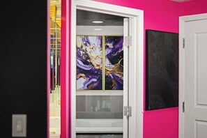 A hallway with a glass door leading to a room, a pink wall, and a framed artwork.