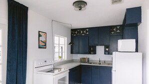 Eine kleine Küche mit Herd, Spüle und Kühlschrank, ausgestattet mit dunkelblauen Schränken und einer weißen Arbeitsplatte.