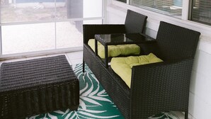 Ein Zimmer mit Deckenventilator, einem großen Fenster mit Jalousien, einem Korbssessel mit Kissen und einem gemusterten Teppich.