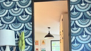 Una habitación con papel tapiz estampado, una mesa de comedor con sillas, una lámpara colgante y una estantería con libros.